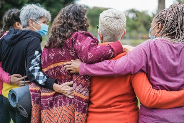 Multi generational women having fun before yoga class wearing safety masks during coronavirus outbreak at park outdoor  Main focus on center senior hair