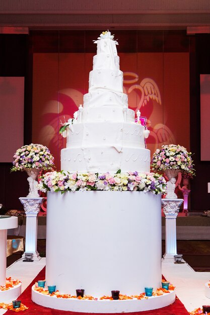 A multi level white wedding cake on a silver base and pink flowers on top