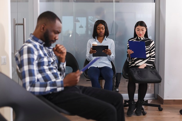 Multi racial job applicants sitting in lobby area of business\
company while reviewing cv resumes before interview series.\
tensioned diverse people in waiting for hr department head manager\
to show up.