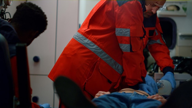 Photo multi racial paramedics providing heart massage to patient in ambulance car emergency care doctors using respiratory mask for ventilation man lungs medical workers giving first aid help to victim