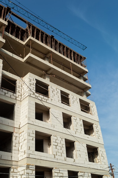 Multi-storey residential building under construction and crane on a background of blue sky