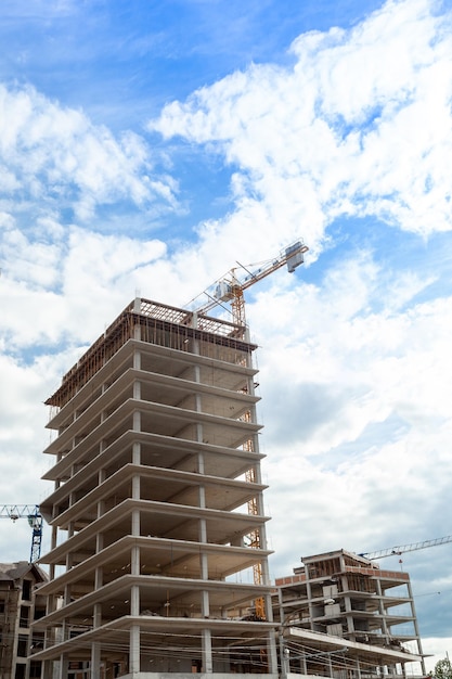 Multi-storey residential building under construction and crane on a background of blue sky