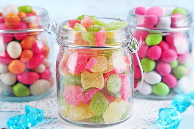 Multicolor candies in glass jars on color wooden background