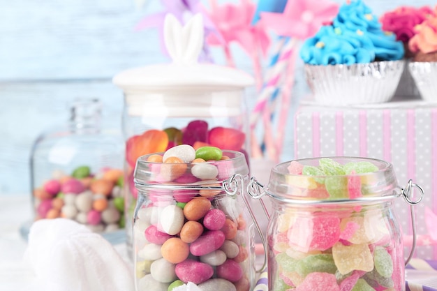 Multicolor candies in glass jars and cupcakes on color wooden background