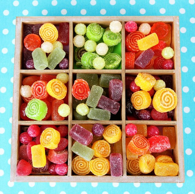 Multicolor candies in wooden box on color background