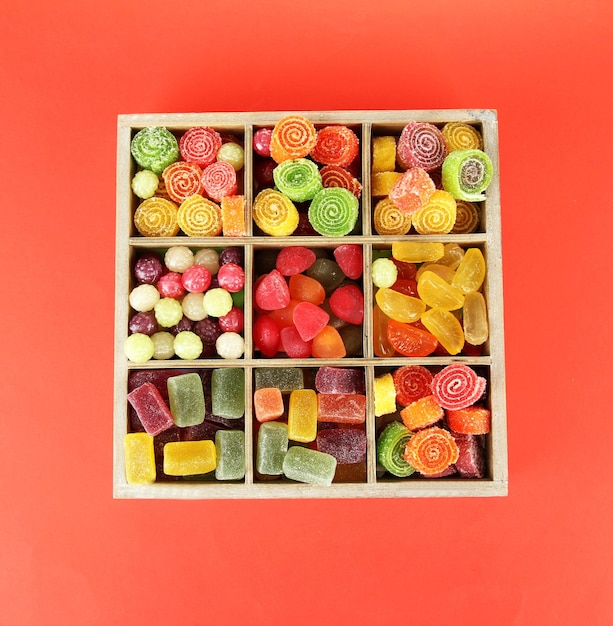 Multicolor candies in wooden box on color background