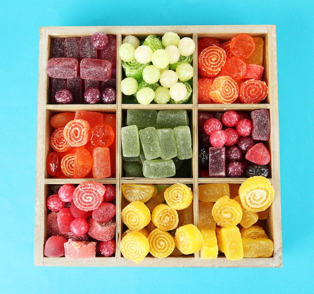 Multicolor candies in wooden box on color background