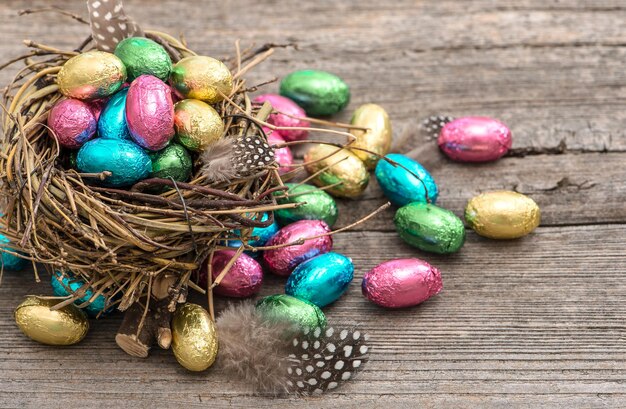 Multicolor chocolate easter eggs in nest on wooden background. Festive still life