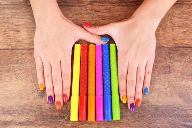 Multicolor female manicure with markers on wooden background