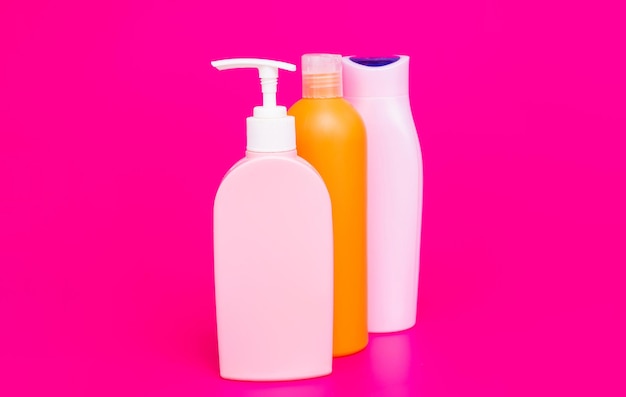 Multicolor plastic liquid containers for cosmetic products packaging in row pink background copy space, bottles.