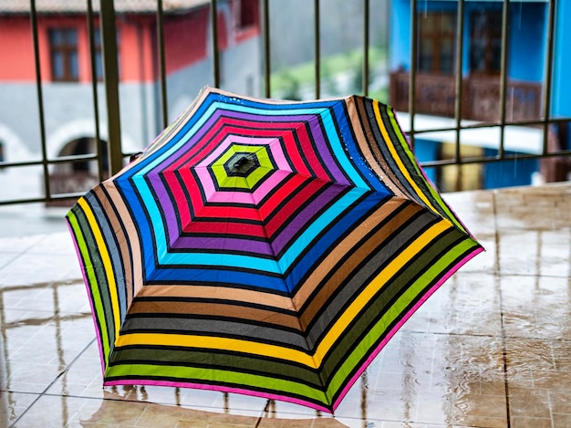 Многоцветный зонт крупным планом в каплях дождя, стоящих на террасе с геометрическим рисунком радуги