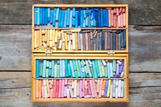 Multicolored art pastel crayons in open wooden artist box on table top view