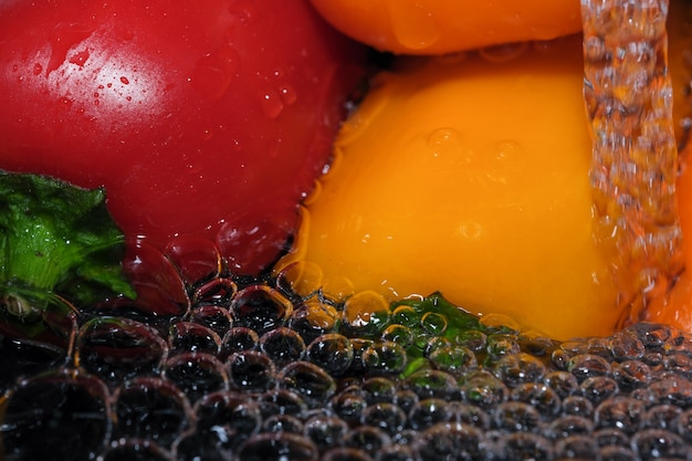 Multicolored bell peppers are washed in clean water close-up macro photography on a black background