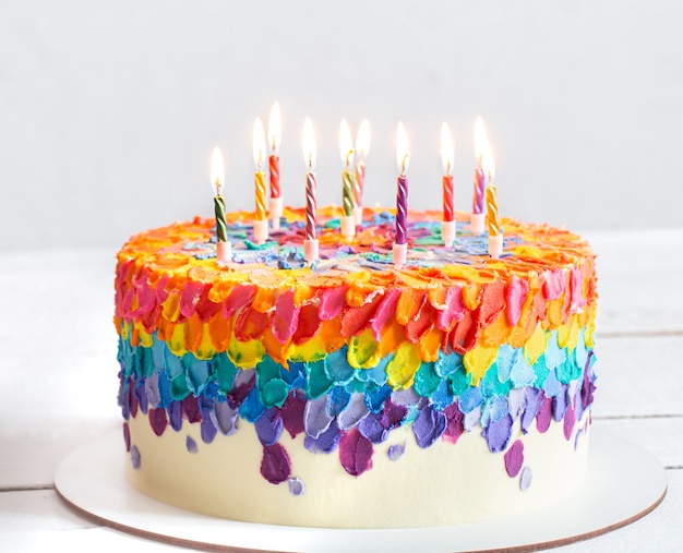 A multicolored birthday cake decorated with burning candles. Happy birthday greetings concept.