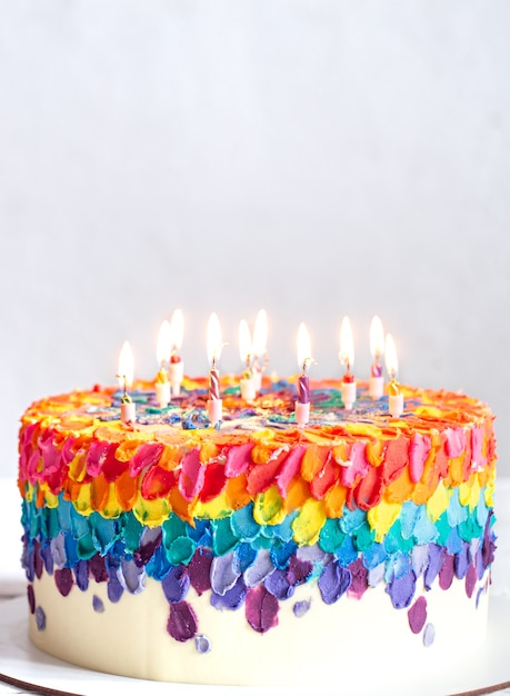 A multicolored birthday cake decorated with burning candles. Happy birthday greetings concept.