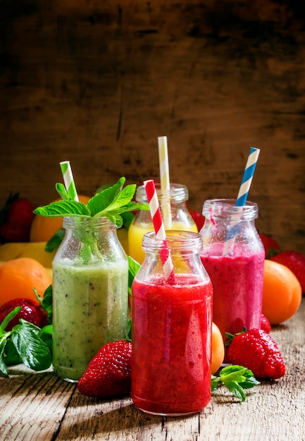 Multicolored bottles with fresh fruit smoothies with striped straws berries fruit and mint leaves vintage wooden background selective focus