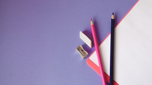 Photo multicolored, bright, colorful pencils are located at the bottom at an angle and a notebook on a violet background