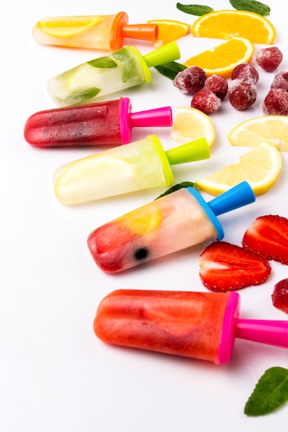 Multicolored bright fruit popsicle with strawberry, cherry, lemon, orange, lemon and mint and slices fresh fruit on a light white