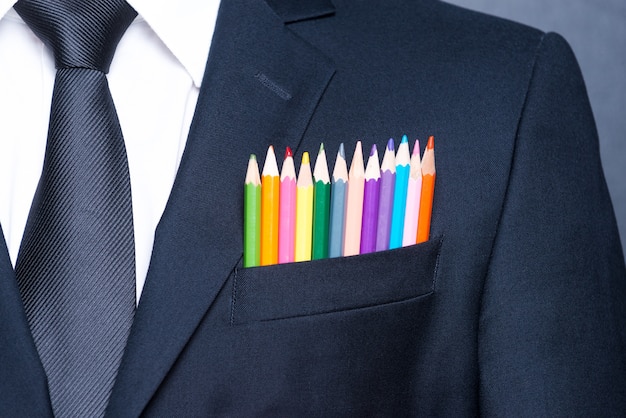 Multicolored businessman.  Close-up of a pocket of businessman with colorful pencils while standing against blackboard