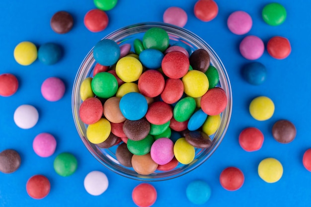 Разноцветные конфеты на ярко-синем фоне в стеклянной тарелке Вид сверху