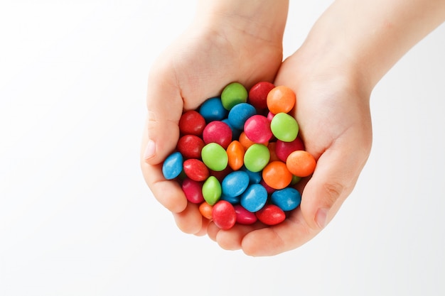 Multicolored candies in the hands of a child on a white background