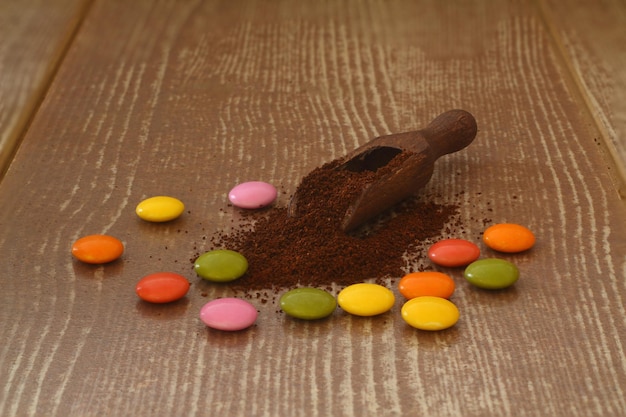 multicolored candy and roasted coffee beans on brown background With wooden spoon