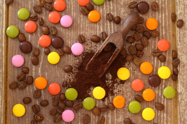 multicolored candy and roasted coffee beans on brown background With wooden spoon