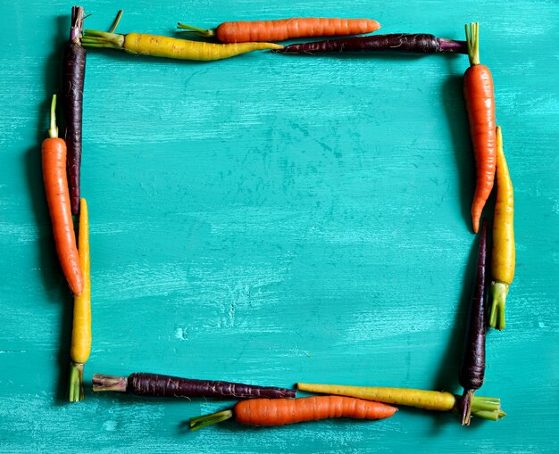 Multicolored carrots framing a square on turquoise colored wood