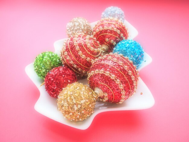 Multicolored Christmas balls on a white plate in the shape of a Christmas tree Pink background with dark vignette Beautiful red silver green yellow blue gold Christmas decorations Soft focus