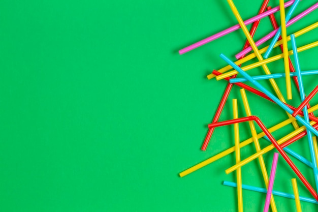 Multicolored cocktail tubes straws on green background