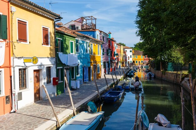 Foto case colorate multicolori a venezia sull'isola di burano canale stretto con barche a motore lungo le case giorno soleggiato estivo focus selettivo