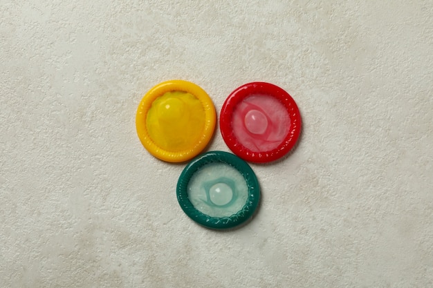 Multicolored condoms on white textured surface