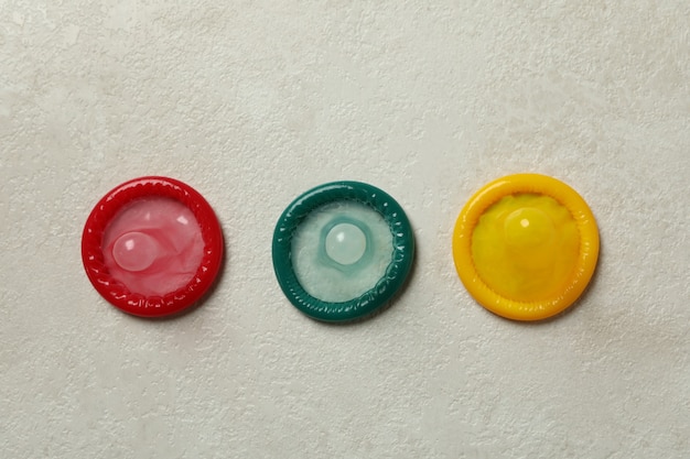 Multicolored condoms on white textured wall, top view