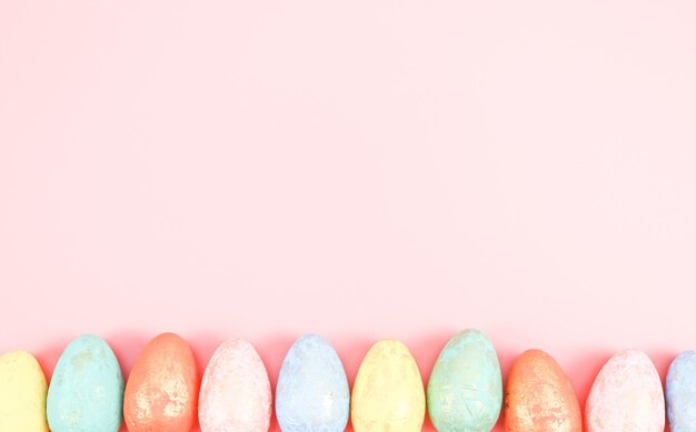 Multicolored decorative pastel colored eggs lie in a row from below on a light pink