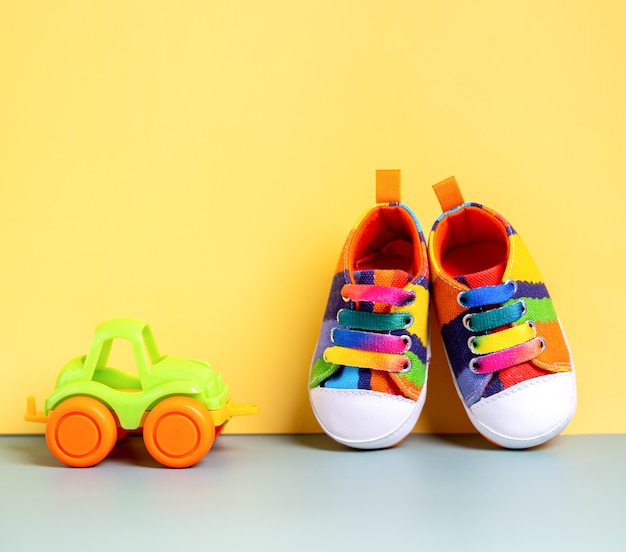 Multicolored denim sports shoes for the baby on a yellow background with a childrens car childrens b...