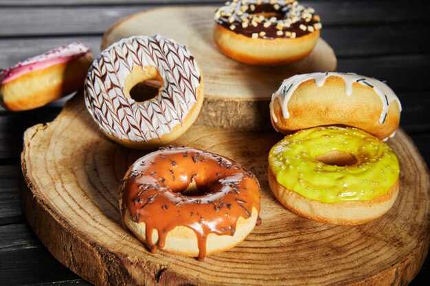 Multicolored donuts with glaze and sprinkles on wooden coasters on a black background.