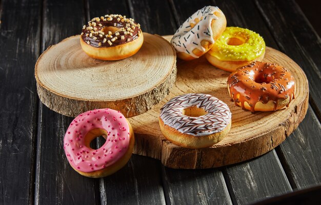 multicolored donuts with glaze and sprinkles on wooden coasters on a black background.