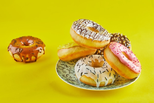 Multicolored donuts with icing and splashes on a blue plate on a yellow background.