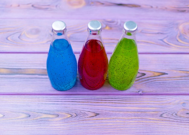 Multicolored drinks with seeds in bottles on a violet wooden background