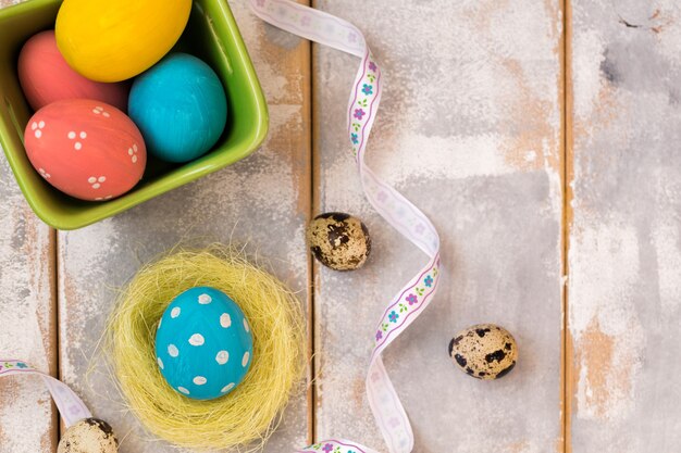 Multicolored Easter eggs in a wooden box and nest ,ribbons on a wooden.