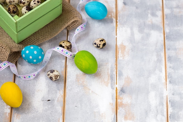 Multicolored Easter eggs in a wooden box, ribbons on a wooden.