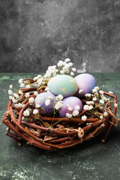 Multicolored eggs for Easter in nest with flowers on green background