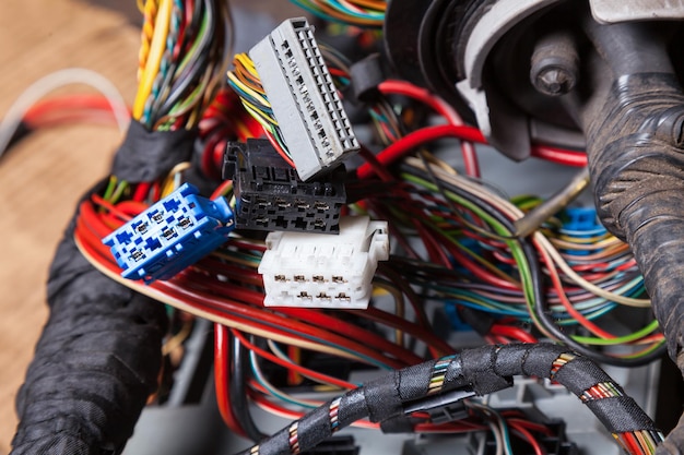 Photo multicolored electrical wires with connectors of white gray and blue colors in the nodes of the car rewound with insulation tape during network repair by an engineer or mechanic in a car service