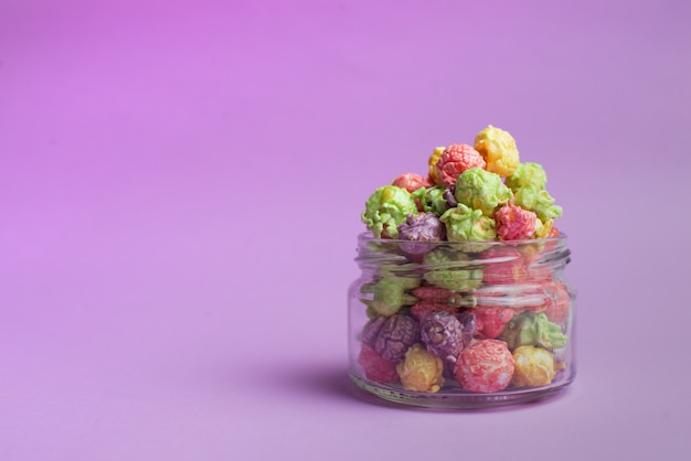 Multicolored fruit flavored popcorn in glass cups on pink background. Candy coated popcorn.
