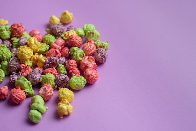 Multicolored fruit op smaak gebrachte popcorn op roze achtergrond. met snoep beklede popcorn.