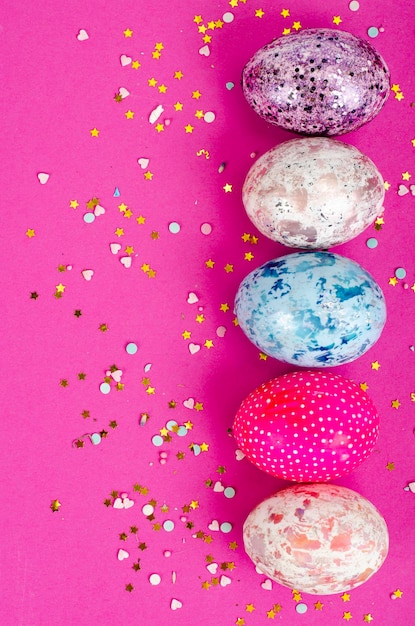 Multicolored handmade easter eggs and confetti on pink background. Minimal concept. View from above. Space for text. Studio Photo