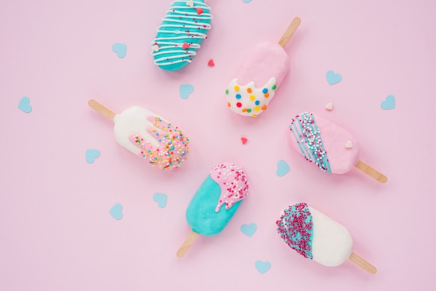 Multicolored ice cream popsicle, covered with confetti on a pink background. View from above