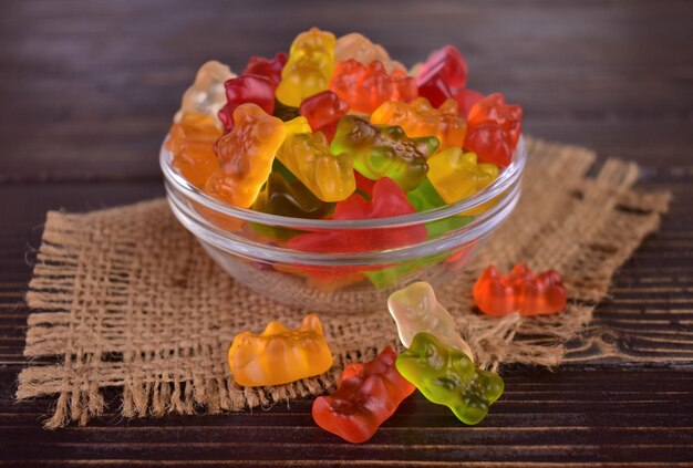 Multicolored jelly bears in a glass bowl on a dark wooden background.