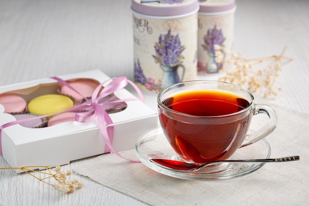 Multicolored macaroons in a box and a cup of tea on a light wood kitchen table Morning tea and swee