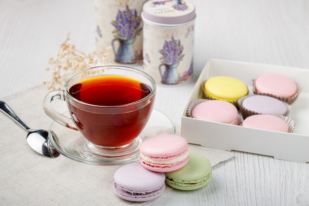 Multicolored macaroons in a box and a cup of tea on a light wood kitchen table